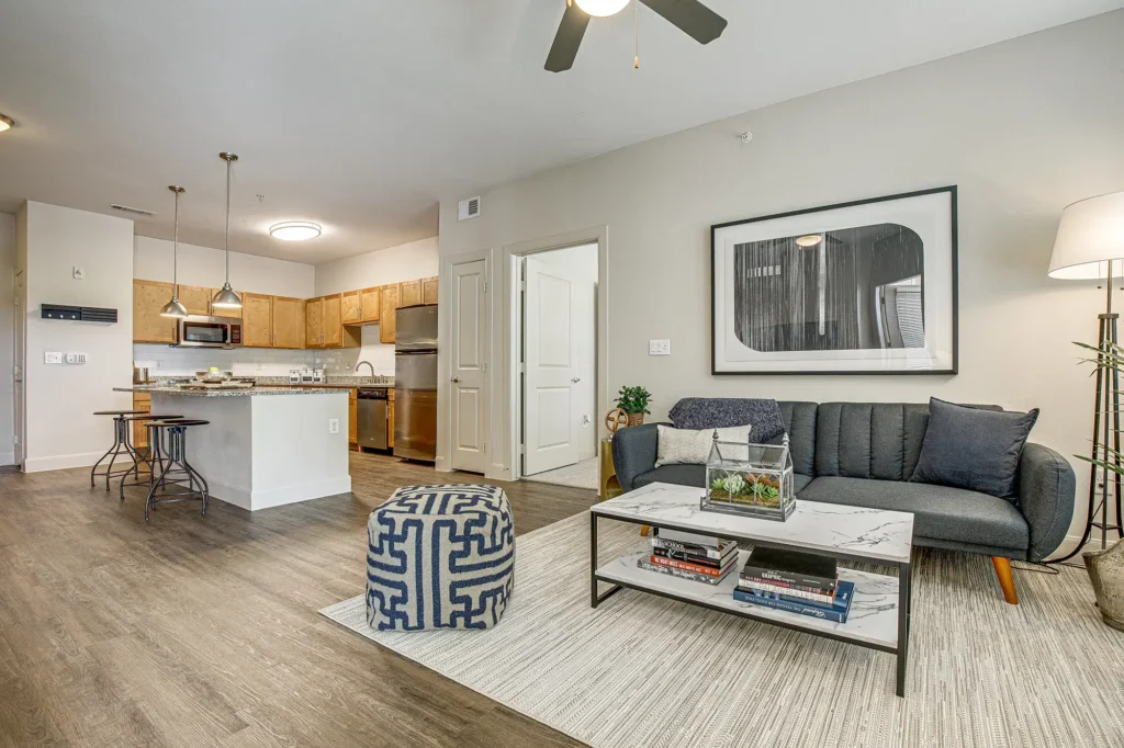 Open living room with large windows and ceiling fan, and view into the kitchen
