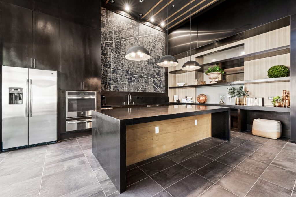 Modern kitchen with black countertops, stainless steel appliances, open shelving, pendant lights, and a large wall map. Decorative plants and books are on the shelves, and the design features clean lines and neutral tones.