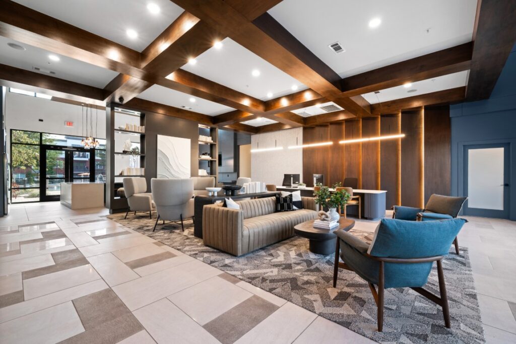 Modern office lobby with wood ceiling beams, stylish seating areas, neutral tones, large windows, and decorative lighting. A reception desk and cozy chairs create a welcoming, contemporary atmosphere.